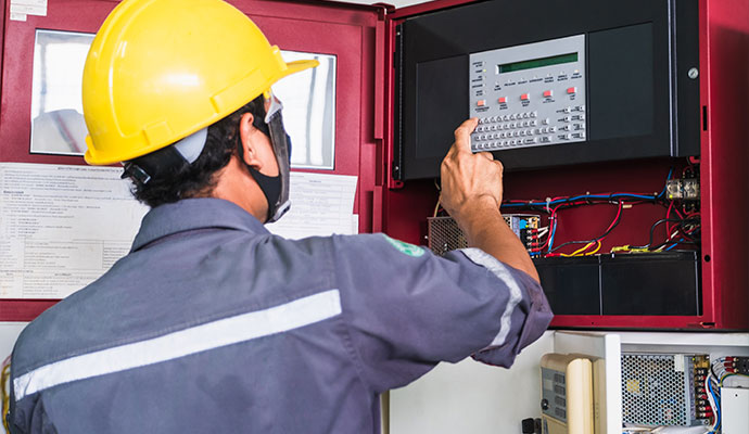 Technician in hard hat operating a fire alarm control panel