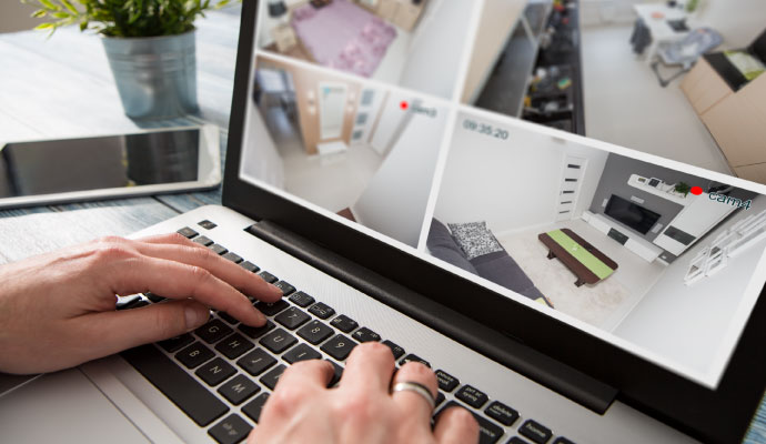 Person monitoring home security camera footage on a laptop