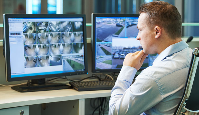 Security operator monitoring multiple surveillance camera feeds on computer screens